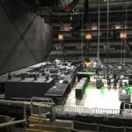 Empty indoor arena with stage and seating areas under setup.