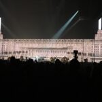 Illuminated grand building with spotlight and dark crowd at night.