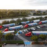 A busy truck parking lot with multiple red trucks and trailers lined up.