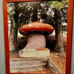 A large red mushroom sculpture on a pedestal in a wooded area.