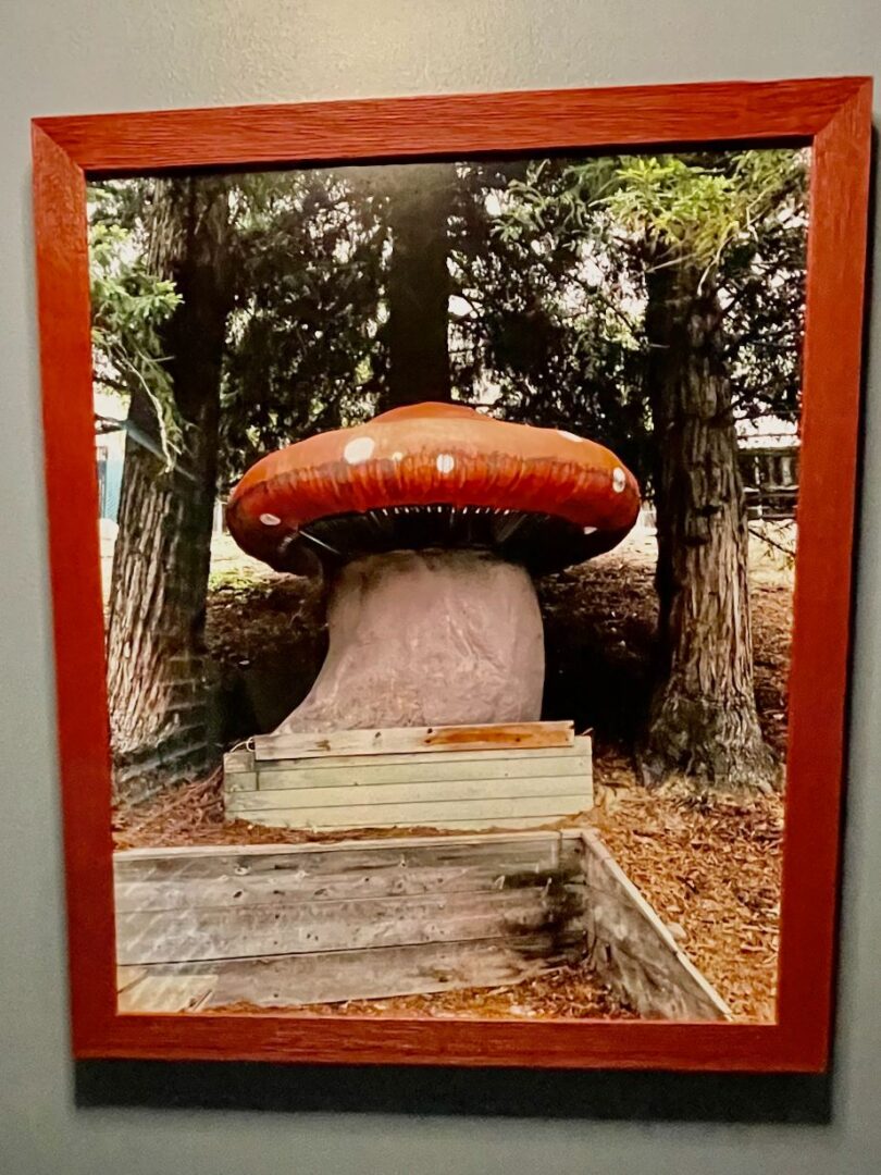 A large red mushroom sculpture on a pedestal in a wooded area.