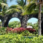 Lush garden with stone arches framed by palm trees under a bright sky.
