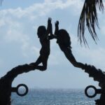 Silhouetted acrobats performing a handstand on curved structures by the sea.