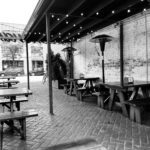 Empty outdoor seating area with wooden benches and string lights.