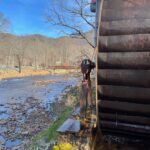 Water wheel beside a river on a clear day with bare trees.