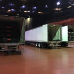 Three large trailers parked inside a spacious warehouse at night.
