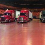 Three semi-trucks parked indoors on a polished floor.