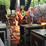 Band performing live on an outdoor stage with vibrant lighting and sound equipment.
