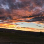 Vibrant sunset with dramatic clouds over open fields.
