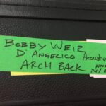 Green label with handwritten names and notes on a black surface.