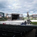 Empty outdoor concert venue with stage and seating under a cloudy sky.