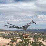 Metal sculpture of a roadrunner in a desert landscape.