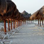 Beach lounge chairs under thatched umbrellas on sandy shore.