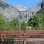 Brown bridge with mountains and greenery under a blue sky.