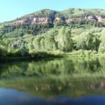 A serene lake reflecting lush green hills and trees under a clear sky.
