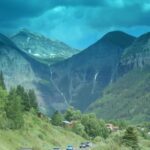 Scenic mountain valley with winding road and vehicles.