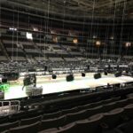 Empty stadium seating with a stage setup and lighting rig in progress.