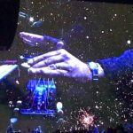 A hand manipulating a futuristic holographic interface with cosmic visuals.