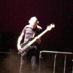 Musician playing bass guitar on a dimly lit stage.