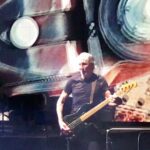 Musician playing bass guitar on stage with dynamic background.