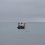 A small colorful boat floating on calm, gray waters under an overcast sky.