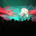 Concert stage with large screen showing hands and a face.